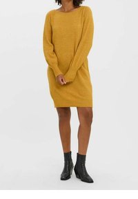 Robe-pull en maille jaune moutarde avec une coupe ample, un col rond et des manches longues. Associée à des bottines noires texturées.