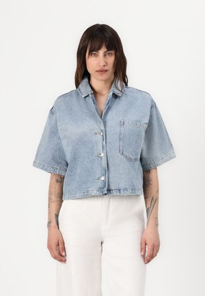 Light blue cropped denim jacket with short sleeves, front buttons, and a single chest pocket. Smooth texture with a relaxed fit.
