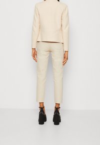 Blazer ajustado de color blanco roto con hombros estructurados, combinado con pantalones slim-fit de color crema claro y tacones de plataforma negros con correas en los tobillos.