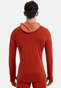 Felpa sportiva a maniche lunghe di un rosso intenso con cappuccio arancione chiaro a contrasto. Realizzata in un tessuto morbido e traspirante con una vestibilità aderente.