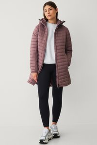 Lichte mauve pufferjack met capuchon, gestikt ontwerp, rits aan de voorkant en zijzakken, gedragen over een grijs vest en zwarte leggings.