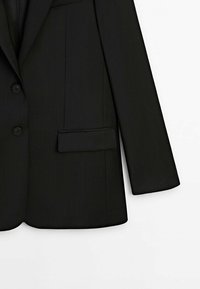 Sort blazer lavet af struktureret stof. Har to knapper, en haket revers og en enkelt brystlomme. Lige snit med skræddersyet pasform.