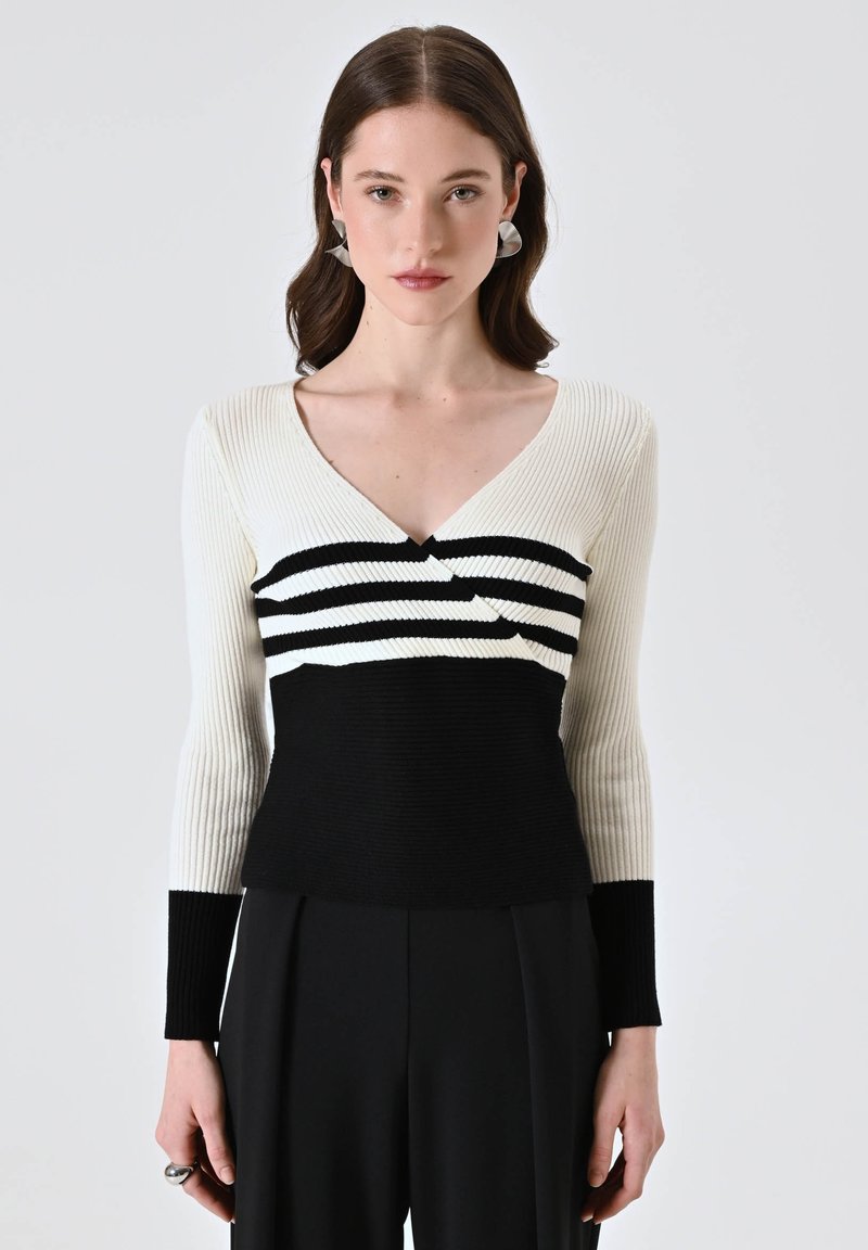 Maglione a coste bianco e nero con scollatura a V, caratterizzato da strisce orizzontali nella zona del petto e una parte inferiore nera uniforme. Maniche lunghe.