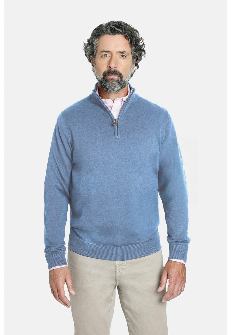 Suéter azul claro con cremallera en el cuello, hecho de un suave tejido de punto. Presenta mangas largas y puños acanalados. Lleva puesto sobre una camisa de color rosa claro con cuello.