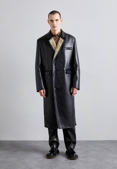 Black leather overcoat with a satin-like texture, double-breasted design, and contrasting shearling lining, paired with matching trousers.