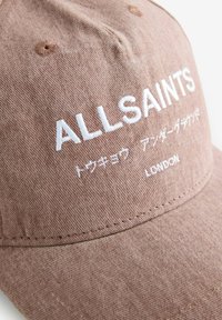 Brun bomullskeps med broderad text "ALLSAINTS" och japanska tecken. Utmärkande grov textur med en böjd skärm.