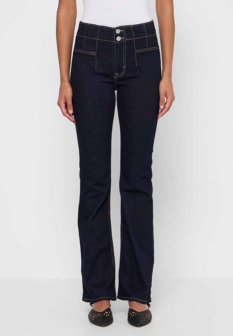 Jeans évasés bleu foncé en denim, avec taille haute, deux poches avant, couture visible et fermeture à glissière avec bouton.