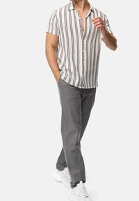 Kurze ärmellose Hemdbluse in Creme mit blauen vertikalen Streifen; kombiniert mit taillierten grauen Hosen und weißen klobigen Sneakers.