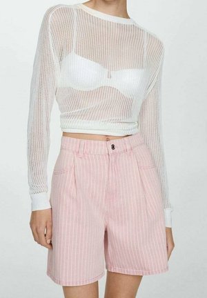 Nainen pukeutunut valkoiseen verkkokudottuun pitkähihaiseen crop toppiin valkoisen rintaliivien päällä ja korkeavyötäröisiin vaaleanpunaiseen pinstripe-shortseihin, joissa on taskut ja napitus.