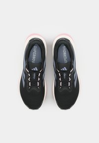Zwarte sportschoenen met een gestructureerde bovenkant, roze accenten op de zool en blauwe strepen. Voorzien van een vetersluiting en een gevoerde binnenzool.