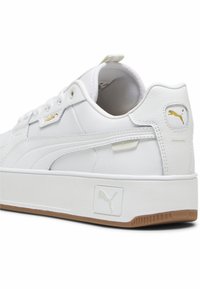 Adidași albi cu un treflex din piele texturată, accente aurii ale logo-ului și o talpă groasă din cauciuc, având o talpă din gumă.