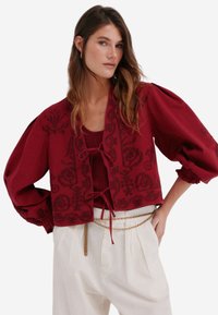 Bordeaux cropped jakke med broderet blomstermønster, bløde ærmer og knyt foran detalje. Kombineret med høj talje cremfarvede bukser.