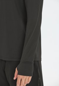 Schwarzes, langärmliges Sportshirt mit strukturiertem Stoff, ausgestattet mit Daumenlöchern an den Bündchen und dezenten Nahtdetails für zusätzlichen Komfort.
