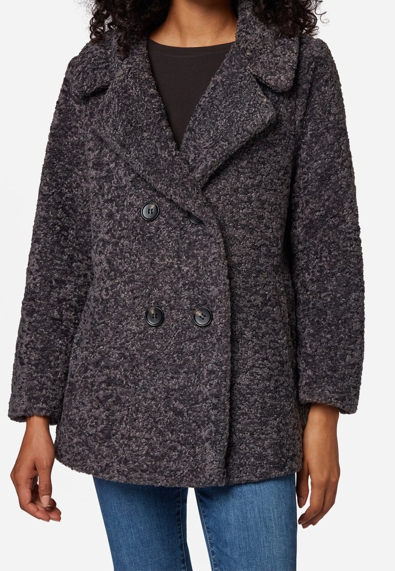 Dwurzędowy szary płaszcz o fakturowanej, puszystej powierzchni, z dużym klapem i czarnymi guzikami, zestawiony z ciemnym topem i niebieskimi dżinsami.