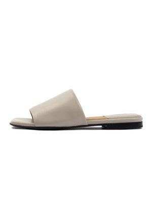 Sandale beige à bout ouvert avec large bride, semelle plate noire et semelle intérieure rembourrée sur fond blanc.