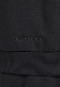 Tessuto atletico nero con una texture a coste. Presenta il logo DRI-FIT in filo coordinato, evidenziando un design aderente e un materiale elasticizzato.