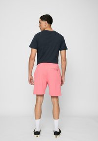 Sort T-shirt med korte ærmer, parret med lyserøde shorts med elastisk talje og baglomme. Model iført hvide sokker og sorte sko.