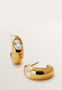 Pendientes de aro dorados con un acento de piedra preciosa clara y facetada. Superficie lisa y pulida con un diseño curvado y cierre de palanca.