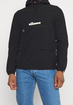 Czarna bluza z kapturem, z przednią kieszenią na zamek i logo "ellesse", noszona z niebieskimi jeansami na stojącej osobie.