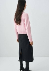 Pull en tricot rose avec des poignets et un ourlet côtelés, associé à une longue jupe noire avec une fente arrière. Les deux vêtements sont simples et épurés.
