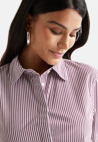 Camicia a righe nei toni del bordeaux e bianco, con colletto, bottoni a vista e una trama di tessuto liscia.