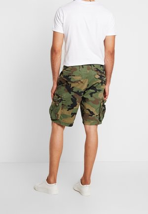 Camouflage cargoshorts med flere sidelommer, lavet af tekstureret stof i grønne og brune nuancer, kombineret med en simpel hvid t-shirt.