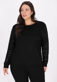 Maglietta nera a maniche lunghe con un corpo liscio e maniche testurizzate con paillettes. Presenta un collo a giro e polsini aderenti.