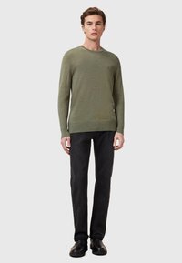 Olijfgroen gebreid sweater met een ronde hals, gecombineerd met zwarte jeans en zwarte schoenen. Soepele textuur en aansluitend ontwerp.