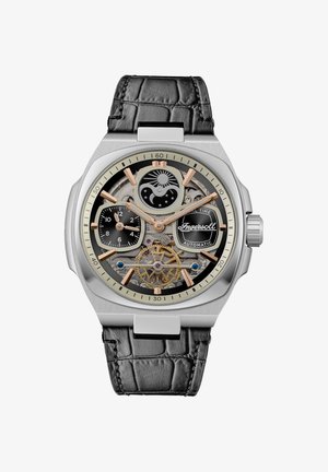 Automatik-Uhr mit Gehäuse aus Edelstahl, schwarzem Krokodillederarmband, silbernen und goldenen Akzenten, transparentem Zifferblatt, das komplexe Mechanik offenbart.