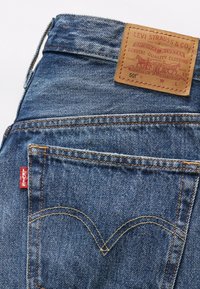 Poche de jean en denim Levi's bleu avec couture orange, étiquette rouge Levi's et étiquette de marque en cuir marron sur la ceinture.