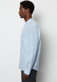 Lichtblauw langslauwe shirt gemaakt van een gestructureerde stof, met een mandarijnen kraag, een borstzak en knoopsluiting bij de mouwen.