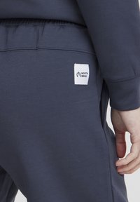 Tmavomodré jogger nohavice s elastickým pásom, bočnými vreckami a malou bielou nálepkou s nápisom "NORTH BEND" vzadu. Mäkka textura.
