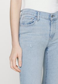 Los jeans de mezclilla azul claro presentan una textura ligeramente desgastada, un diseño tradicional de cinco bolsillos y un cierre de cremallera con botón.