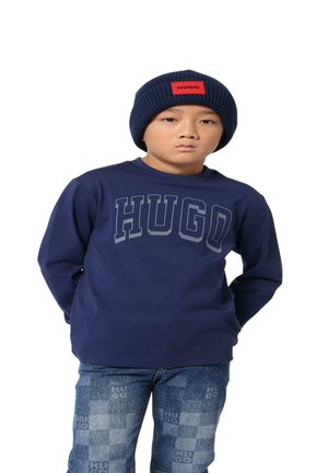 Maglietta a maniche lunghe navy con la scritta "HUGO" stampata in grigio, abbinata a jeans di denim con motivo a scacchi e dettagli con il logo "HUGO".