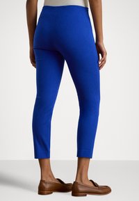 Kraljevsko modre pajkice do gležnjev z gladko teksturo in visokim pasom, kombinirane s rjavimi loaferji.