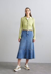 Light green ribbed cardigan, white shirt underneath, and a denim midi skirt with a flared design. Paired with white and gold sneakers.