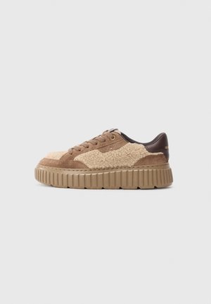 Sneakers with a textured tan and brown upper, featuring suede and shearling materials. Thick ridged beige sole with gold accent detailing.