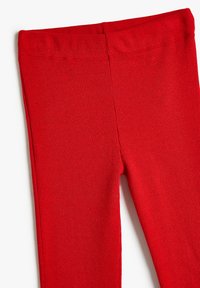 Primer plano de unas mallas de tela de canalé rojo que muestran la cinturilla elástica y la parte superior del muslo contra un fondo blanco.