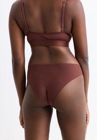 Soutien-gorge de sport marron et culotte assortie, avec un design sans couture et une texture lisse, des bretelles ajustables visibles et une coupe mi-haute.