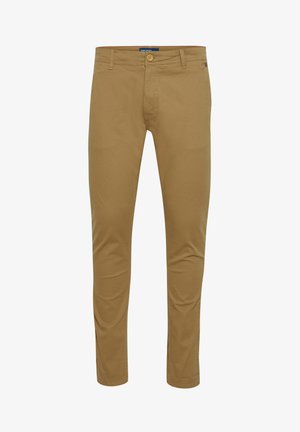 Man draagt lichtbruine casual broek met zijzakken, gedeeltelijk zichtbare witte blouse, handen rusten nabij de zakken.