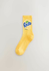 Yellow cotton sock with ribbed cuff featuring a blue and green Fanta logo and "LEMON" text, smooth texture, and standard shape.
