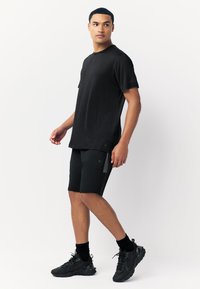 Fekete, rövid ujjú sportpóló fekete rövidnadrággal, finom textúrával, az öltésnél lévő logóval és elegáns, testhezálló szabással.