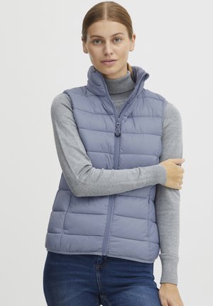 Doudoune bleue claire avec un col montant, fermeture éclair à l'avant et design matelassé. Portée sur un pull à col roulé gris, associée à un jean bleu.