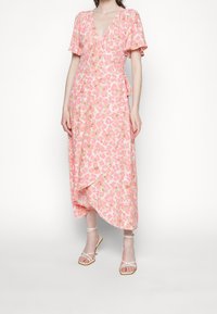 Vestido envolvente floral rosa con mangas cortas con volantes, escote en V y dobladillo asimétrico. Combinado con sandalias blancas de tiras.