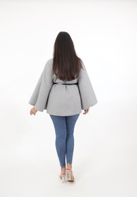 Top gris, texturizado, estilo envolvente con mangas anchas, ceñido en la cintura, combinado con jeans ajustados azules y sandalias de tacón cuadrado transparente.