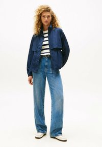 Granatowa, lekka kurtka nałożona na białą bluzkę w granatowe paski, w połączeniu z wysokim stanem szerokimi niebieskimi dżinsami i białymi butami.