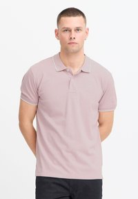 Polo de color rosa claro con un acabado texturizado, ribete gris en el cuello y las mangas, y un pequeño logo en el pecho.
