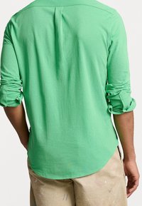 Grön långärmad skjorta i mjukt tyg med uppvikta ärmar, ryggslits och rundad fåll, i kombination med ljusbeiga byxor med färgstänk.