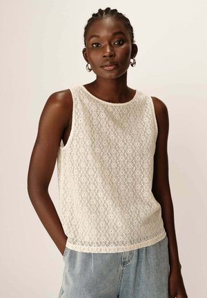 Débardeur en dentelle blanche avec un col rond, présentant des motifs floraux et une texture transparente, associé à un short en denim ample.