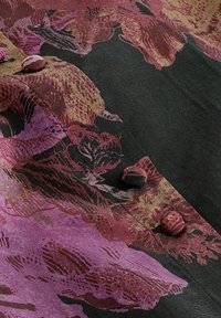 Textile features a floral pattern in shades of pink, maroon, and gold on a black background, with three fabric buttons along the edge.